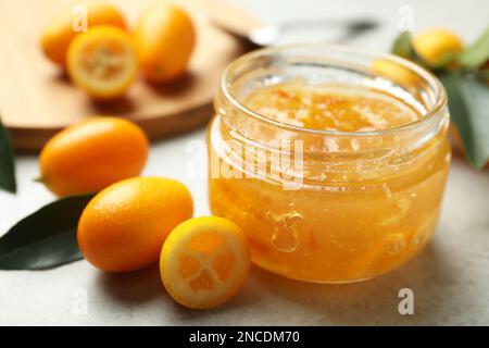 Deliziosa marmellata di kumquat in vaso e frutta fresca su tavolo grigio chiaro, primo piano. Spazio per il testo Foto Stock