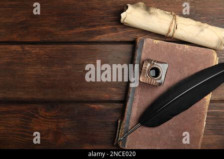 Penna piuma, Inkwell, vecchio libro e pergamena su tavola di legno, piatto. Spazio per il testo Foto Stock