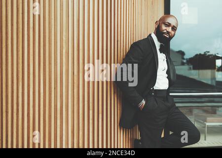 Un uomo nero dandy con una testa calva, che indossa un tuxedo nero, una cravatta d'arco e una camicia bianca; le mani nelle sue tasche, e l'altra mano appoggia il suo corpo su una W. Foto Stock