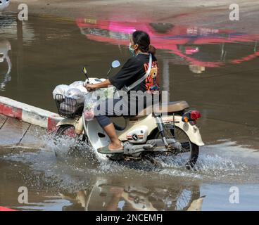 SAMUT PRAKAN, THAILANDIA, 25 2023 GENNAIO, Una donna con borse per lo shopping cavalca una moto attraverso la pozza Foto Stock