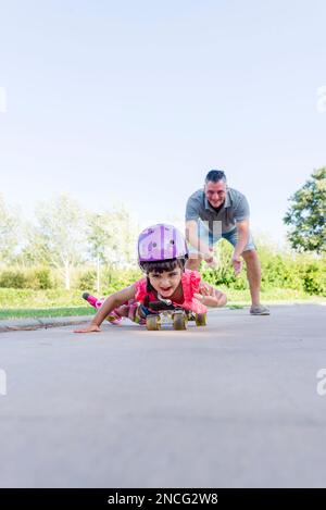 Ragazza che gioca con il padre mentre pattina a rotelle all'aperto nel parco. Foto Stock