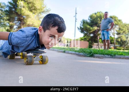 Il bambino gioca con il padre mentre pattina a rotelle all'aperto nel parco. Foto Stock