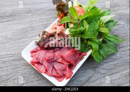 carne di manzo cruda taglia fette su piatto bianco e verdure fresche carne fresca vista dall'alto - sashimi di manzo, fegato di manzo cibo asiatico tailandese Foto Stock