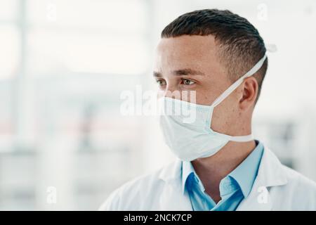 Lo sviluppo di una cura miracolosa richiede un serio lavoro mentale. un giovane scienziato che indossa una maschera e che guarda attento in un laboratorio moderno. Foto Stock