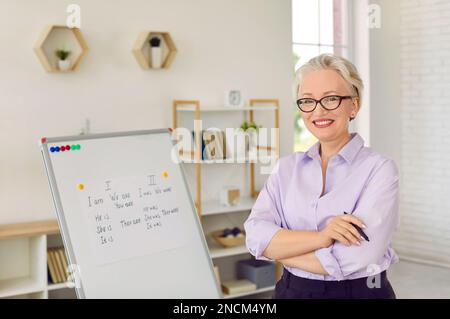 Ritratto di amichevole insegnante di inglese senior in aula vicino alla lavagna. Foto Stock