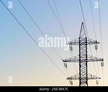 L'estremità di punta dei supporti di ancoraggio delle linee elettriche aeree costa con fili e fasci di trefoli di isolatori ad alta tensione contro i blu trasparenti Foto Stock