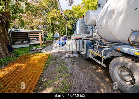 Versando calcestruzzo fresco dal camion miscelatore, l'operaio di costruzione sta dirigendo il tubo della pompa nella giusta direzione, versando lo strato di calcestruzzo sulla costruzione Foto Stock