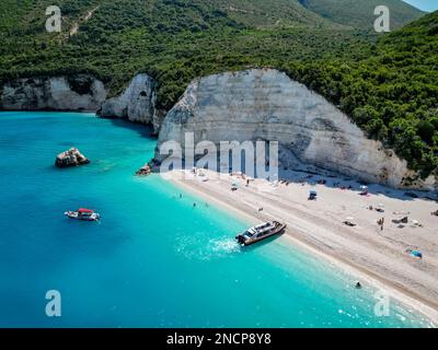 4K lontano fuco di Fteri Beach, Cefalonia, Cefalonia, Grecia con la collina calcarea, taxi in barca e la gente prendere il sole Foto Stock