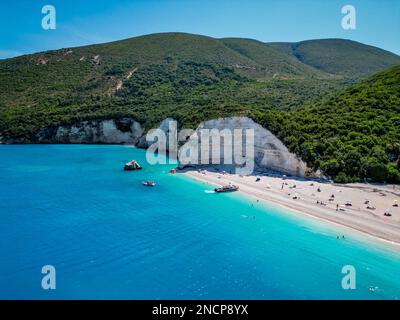4K lontano fuco di Fteri Beach, Cefalonia, Cefalonia, Grecia con la collina calcarea, taxi in barca e la gente prendere il sole Foto Stock