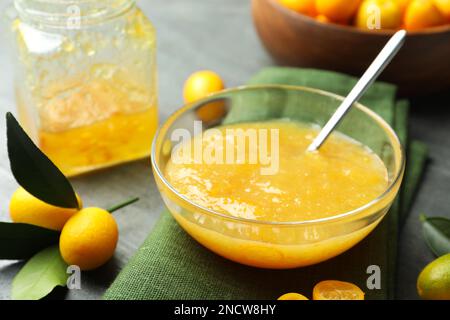 Deliziosa marmellata di kumquat in ciotola e frutta fresca sul tavolo grigio, primo piano Foto Stock