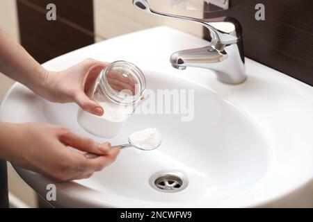 Donna che usa bicarbonato di sodio per disintasare lo scarico del lavandino in bagno, primo piano Foto Stock