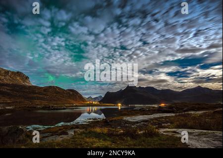 L'aurora boreale attraverso le nuvole nel suggestivo paesaggio montano, Flakstad, Lofoten, Nordland, Norvegia Foto Stock