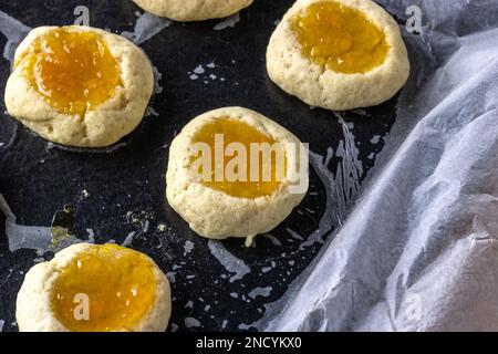 Biscotti con stampa pollice riempiti di marmellata cotta a metà su una teglia da forno da vicino Foto Stock