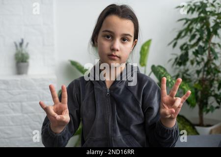 Carino sordomuto ragazza utilizzando il linguaggio dei segni su sfondo chiaro Foto Stock