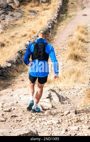 Giovane uomo che pratica il sentiero che corre in alta montagna, mentre scende lungo la montagna Foto Stock