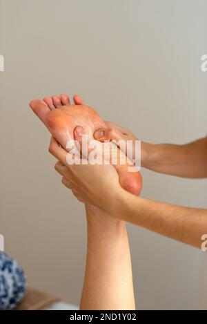 Raccolto anonimo terapista massaggiando piede del cliente in salone termale durante la sessione di riabilitazione Foto Stock