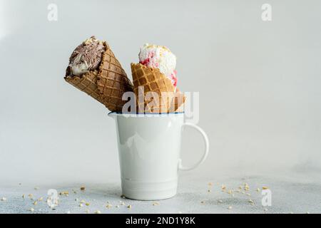 Tazza bianca con coni di waffle riempiti di gelato su un tavolo di cemento Foto Stock
