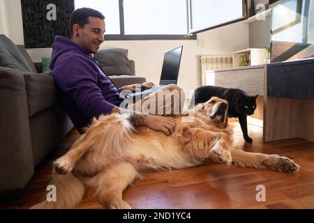Il proprietario è un uomo che si siede sul pavimento con un computer portatile e accarezza il cane mentre lavora lontano da casa Foto Stock