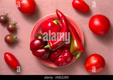Pomodori freschi e peperoni rossi giacenti su un piatto, sfondo rosa. Vista dall'alto. Foto Stock