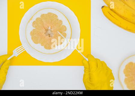 L'uomo mangia il suo pranzo. L'uomo in guanti di gomma tiene coltello e forchetta, taglia pomelo frutta. Vista dall'alto Foto Stock