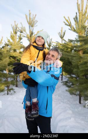 Ragazza prescolare felice che indossa abiti caldi e cappello seduto a spalla del padre durante le vacanze invernali nella foresta innevata Foto Stock