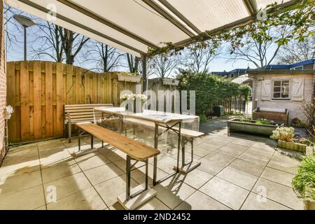 Tavolo di legno con panchine poste vicino recinzione di legno su terra piastrellata nel cortile del cottage suburbano Foto Stock