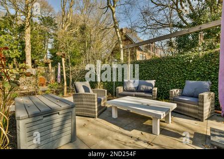 Comodo divano e poltrone posti vicino al tavolo contro il verde cespuglio in giardino con alberi e piante sotto il cielo blu Foto Stock