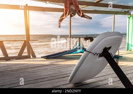 Primo piano aliscafo surf bordo kite attrezzatura sul molo in legno molo Jetty riva sport acquatici spot luminoso giorno di sole contro mare oceano costa con molti kiter Foto Stock