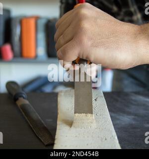 Immagine delle mani di un artigiano che tiene il martello e lo scalpello di un falegname mentre fa un po' di lavoro e di intaglio sul legno. Lavori fai da te in laboratorio. Foto Stock