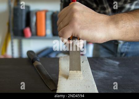 Immagine delle mani di un artigiano che tiene il martello e lo scalpello di un falegname mentre fa un po' di lavoro e di intaglio sul legno. Lavori fai da te in laboratorio. Foto Stock