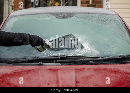 Mano con guanti che tiene un raschietto per ghiaccio, rimuovendo il ghiaccio dal parabrezza anteriore di un'auto ghiacciata. REGNO UNITO Foto Stock