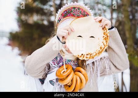 Festa nazionale russa Maslenitsa, shrovetide. Piccole belle ragazze carine in Headscif mangiare grandi frittelle gustose, divertirsi in vacanza frittella inverno Foto Stock