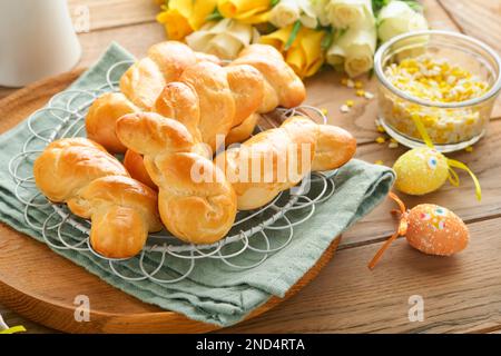 Colazione di Pasqua, concetto di Holliday. Panini di coniglietto pasquale con cannella a base di pasta di lievito con smalto arancione, decorazioni pasquali, uova colorate Foto Stock