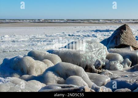 Primo piano della costa ghiacciata, delle onde ghiacciate, delle rocce e del sole che si abbagliano sul ghiaccio Foto Stock