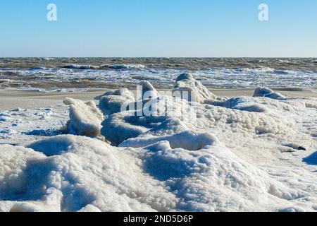 Primo piano della costa ghiacciata, delle onde ghiacciate, delle rocce e del sole che si abbagliano sul ghiaccio Foto Stock