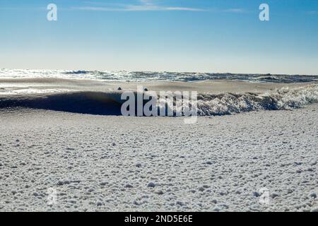 Primo piano della costa ghiacciata, delle onde ghiacciate, delle rocce e del sole che si abbagliano sul ghiaccio Foto Stock