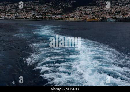 la nave da crociera si sveglia mentre la nave lascia Funchal, Madeira. Funchal è sullo sfondo. L'acqua era bianca e blu. Foto Stock