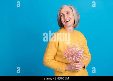 Ritratto di allegro bella persona mani tenere fiori guardare spazio vuoto toothy sorriso isolato su sfondo di colore blu Foto Stock