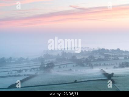 Il paesaggio invernale ghiacciato a nord di Almscliffe Crag è lentamente sommerso dalla nebbia in aumento, mentre un'alba colorata produce colori vividi nel cielo sopra. Foto Stock