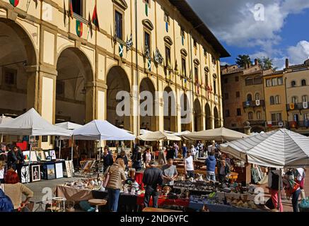Fiera dell'antiquariato di Arezzo (Fiera dell'antiquariato) che si tiene in Piazza grande, Arezzo, Toscana, Italia. L'immagine presenta venditori sotto tende bianche che vendono oggetti d'epoca e oggetti da collezione di fronte allo storico portico Logge Vasari decorato con colorati striscioni in stile medievale. Foto Stock