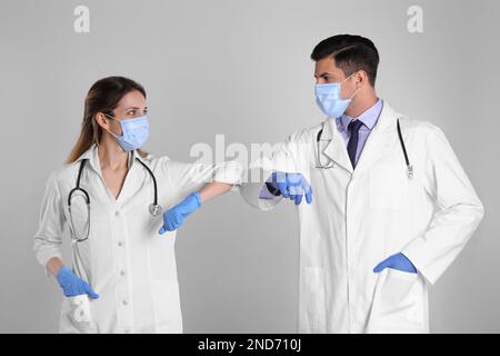 I medici si salutano a vicenda saltando i gomiti invece di fare una stretta di mano su sfondo grigio chiaro Foto Stock