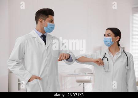 I medici con maschere protettive si salutano a vicenda saltando i gomiti invece di stretta di mano in clinica Foto Stock