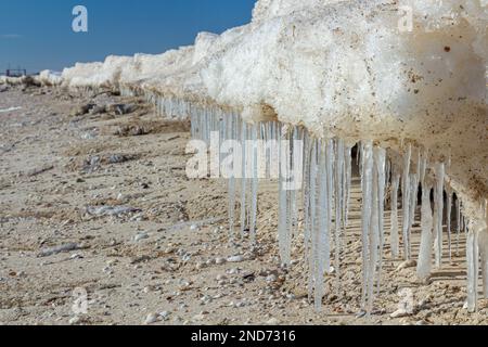 Primo piano della costa ghiacciata, delle onde ghiacciate, delle rocce e del sole che si abbagliano sul ghiaccio. Foto Stock