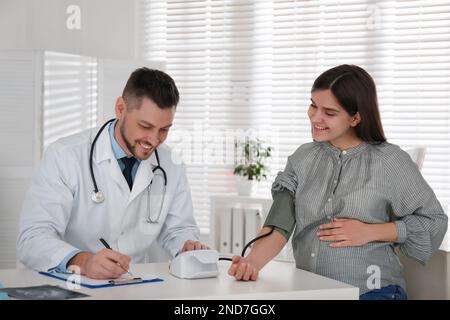 Medico che misura la pressione sanguigna di una donna incinta in clinica Foto Stock