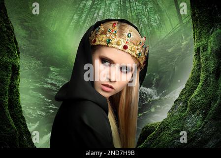 Strega che indossa il mantello nero e la corona nella foresta nebbiosa. Carattere fantasy spaventoso Foto Stock
