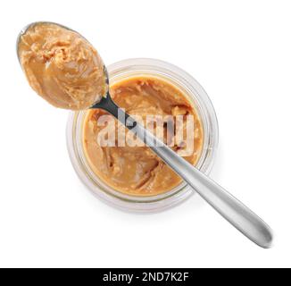 Vaso di vetro e cucchiaio con gustoso burro di arachidi isolato su bianco, vista dall'alto Foto Stock