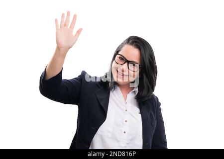 Donna imprenditore adulto con espressione amichevole sorridente indossando occhiali e tuta formale che agita mano come gesto del saluto isolato su bianco studio bac Foto Stock