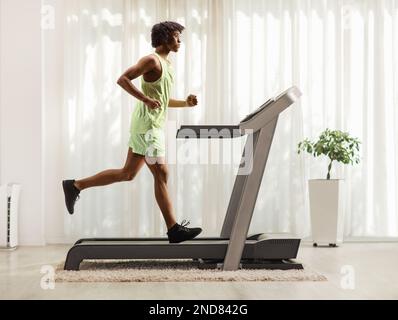 Full lunghezza profilo girato di un ragazzo afroamericano in esecuzione su un tapis roulant a casa Foto Stock