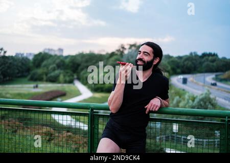 Giovane uomo con una gamba protesica che riposa dal fare sport con il suo smartphone. Concetto: Superamento, sport, tecnologia Foto Stock