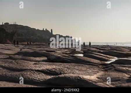 Uno splendido paesaggio naturale al tramonto, caratterizzato da una piacevole passeggiata lungo la pittoresca costa di Sirmione. Le silhouette del Foto Stock